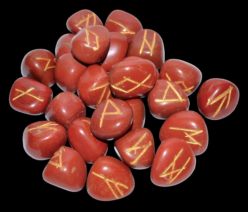 A collection of red jasper rune stones with gold enamel accents, featuring various rune symbols etched into their surfaces.